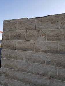 A close-up of a light gray brick wall with unevenly aligned bricks; one brick near the top is noticeably misaligned compared to the others. The sky is clear in the background.
